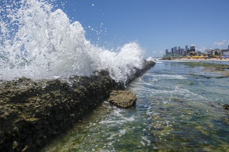 Recife(PE), 24/10/2023 - Explosão de ondas nos recifes costeiros na praia do Buraco da Véia, com a orla de Boa Viagem ao fundo, funcionando como barreira natural. As formações rochosas absorvem até 96% do impacto das ondas.  Foto: Fernando Frazão/Agência Brasil