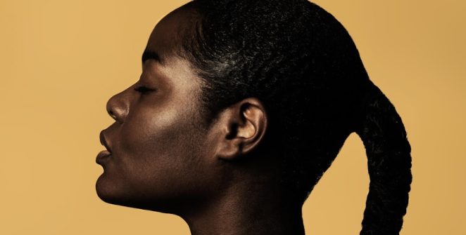 braided woman taking photo beside yellow painted wall