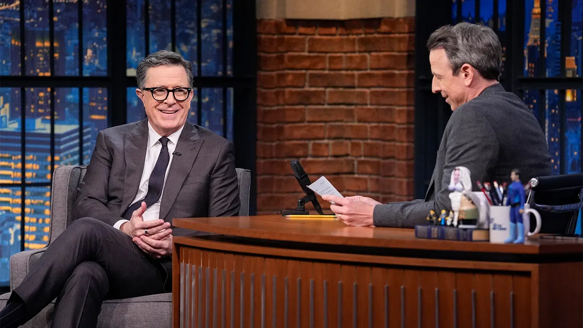Stephen Colbert speaking during an interview with host Seth Meyers on a television set