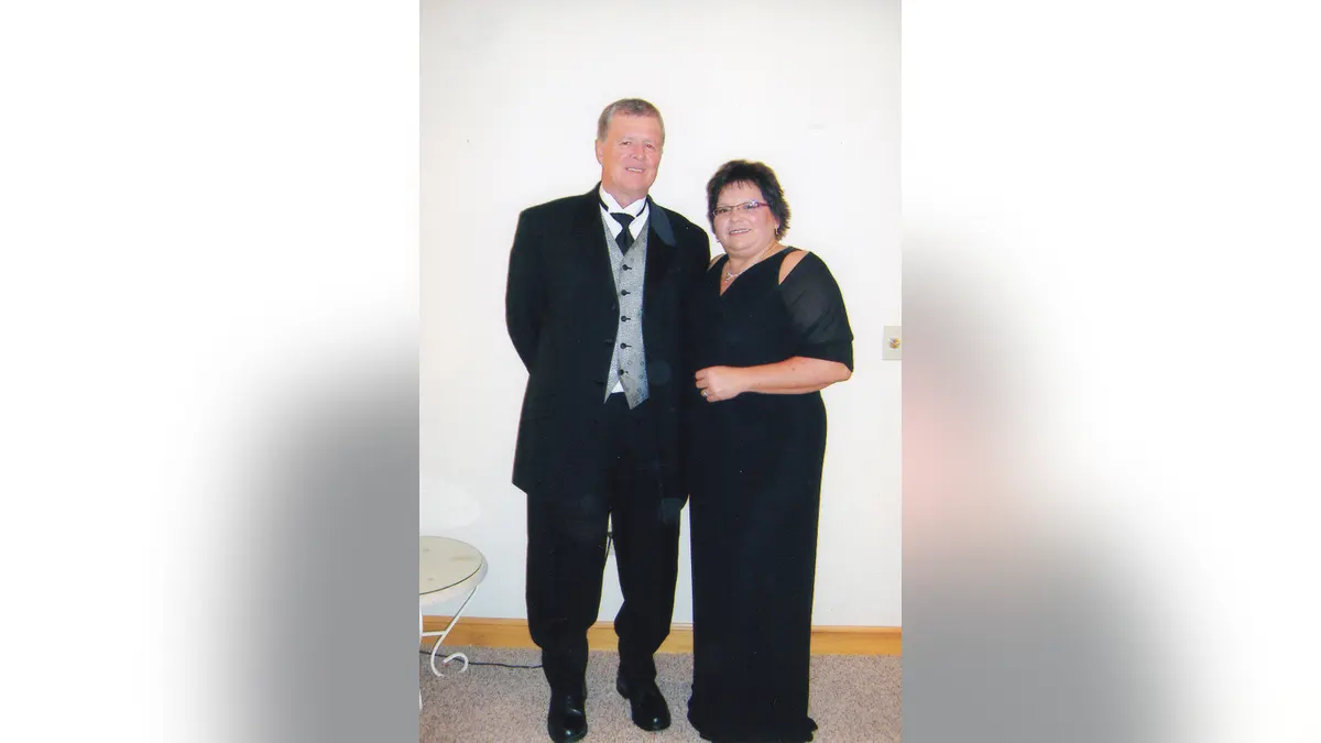 Jeff Walton and Deb Proctor wearing black formal attire against a white wall.