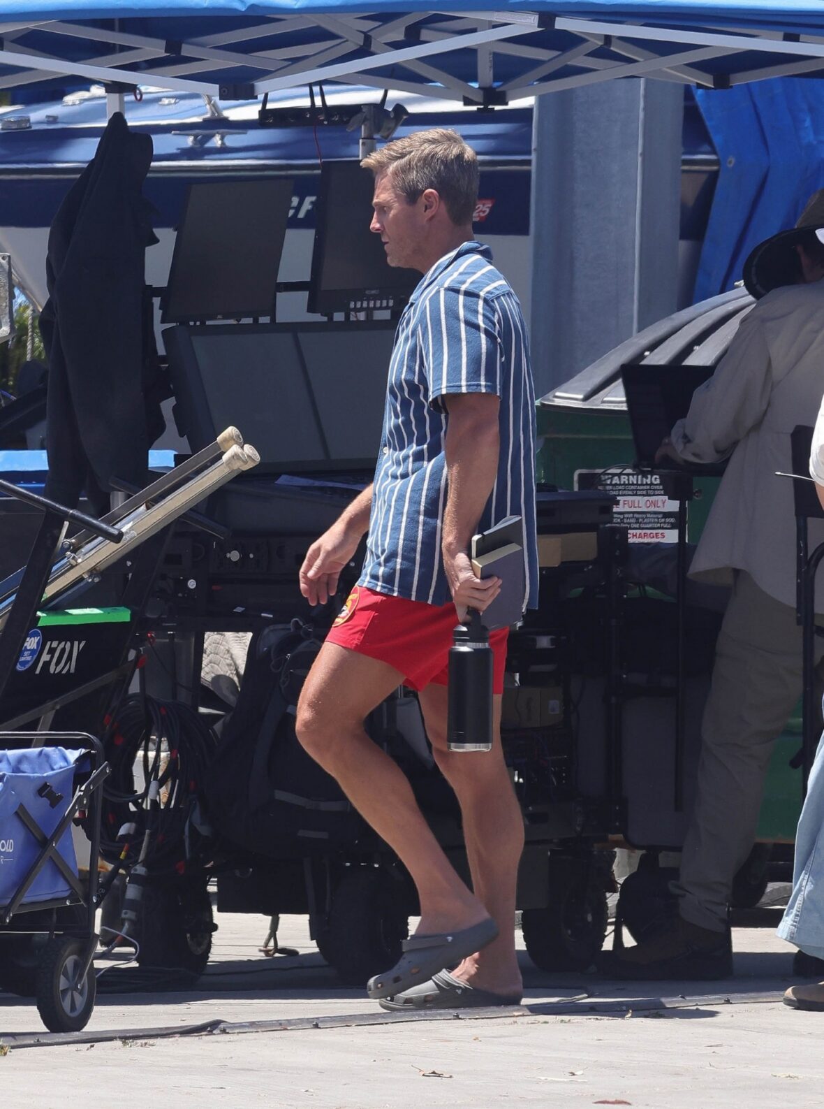 Stephen Amell chega ao set de BAYWATCH com o icônico calção de banho vermelho e camisa listrada