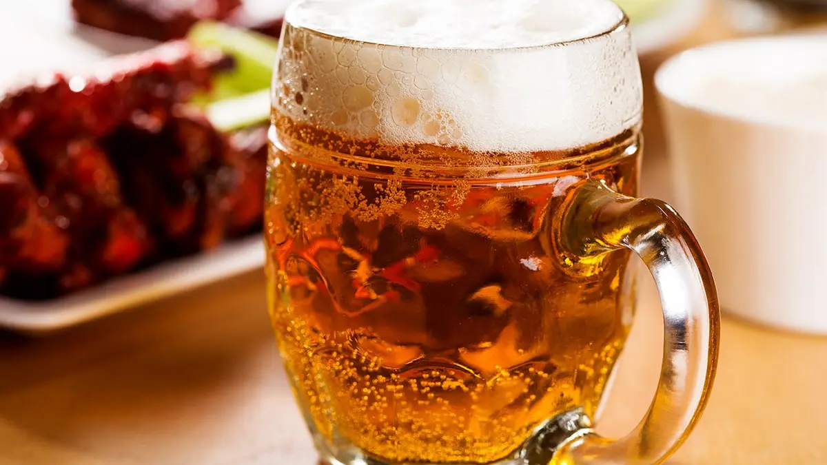 A mug of beer sits beside a plate of food.