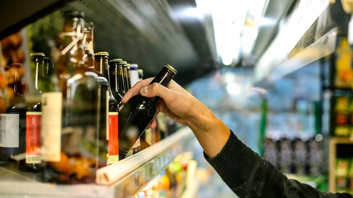 A man selects a bottle of beer from a store shelf.