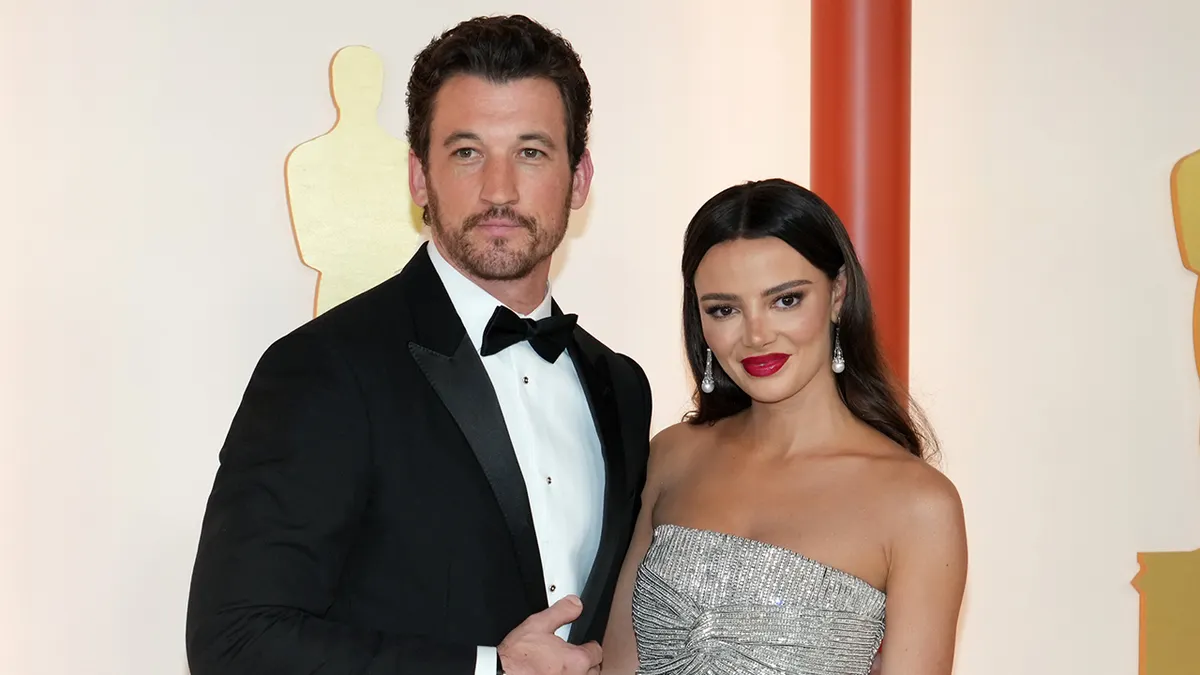 Miles Teller smiling in a tuxedo with wife Keleigh Teller in a silver gown at the Oscars