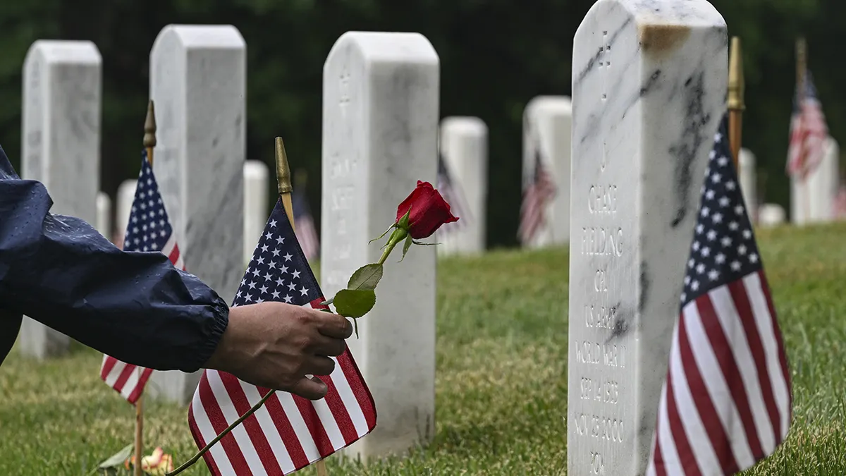 A person laying a rose on a soldier's grave at Arlington National Cemetery