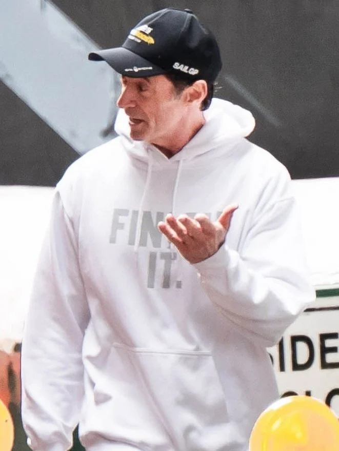Hugh Jackman com capuz branco e a mão levantada