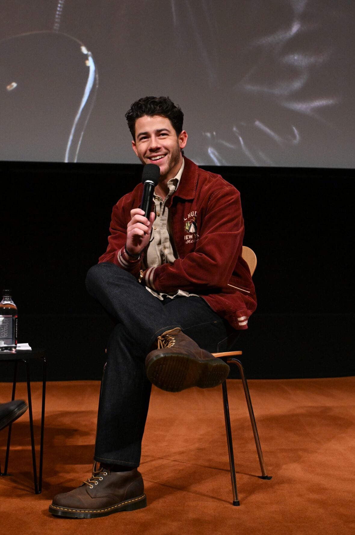 Nick Jonas usa jaqueta bomber cor de vinho para sessão fotográfica de exibição do POWER BALLAD