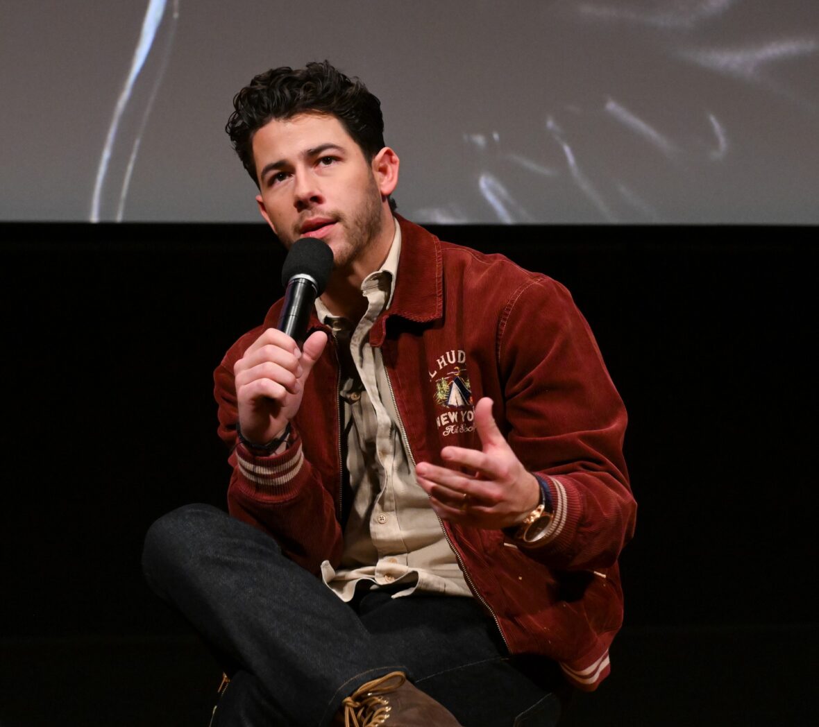 Nick Jonas usa jaqueta bomber cor de vinho para sessão fotográfica de exibição do POWER BALLAD