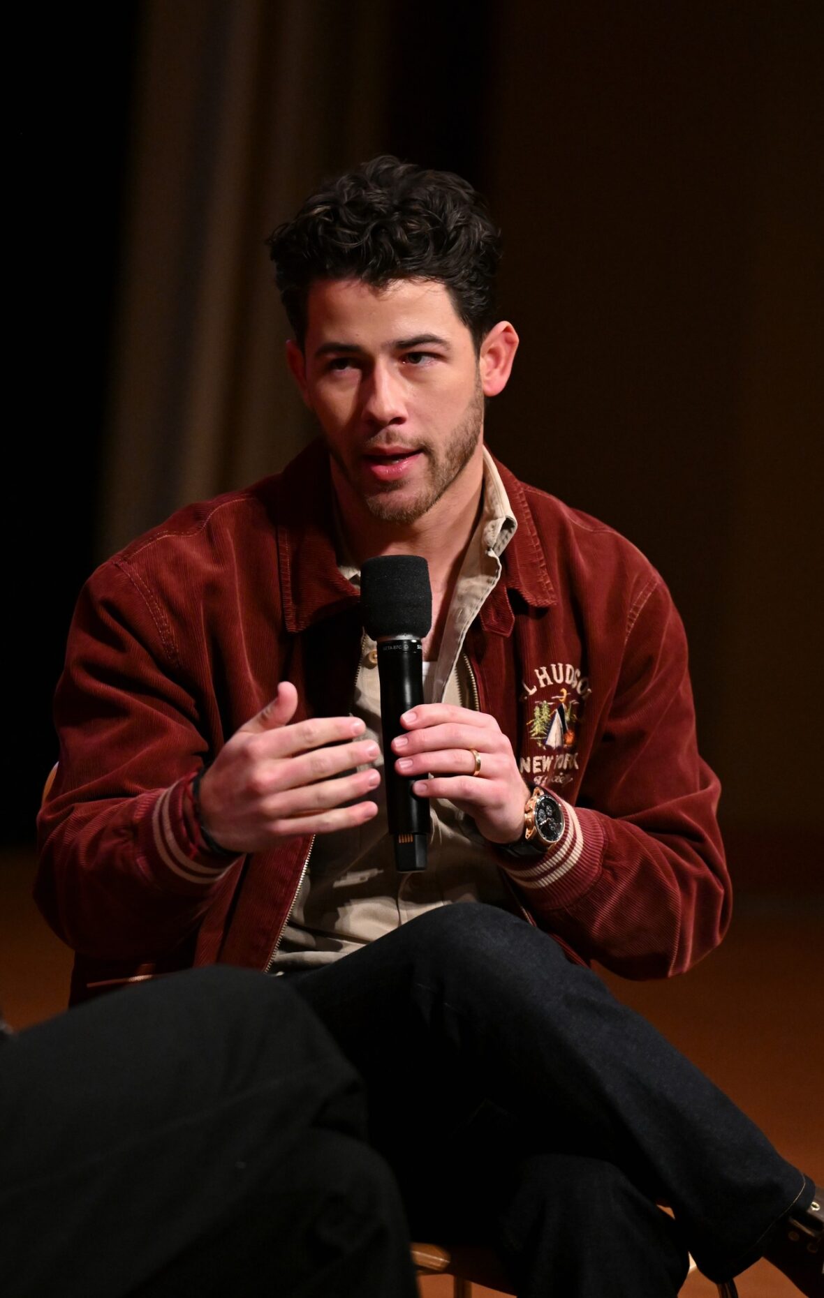 Nick Jonas usa jaqueta bomber cor de vinho para sessão fotográfica de exibição do POWER BALLAD