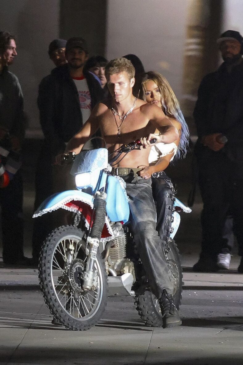 Karol G em uma motocicleta com um modelo masculino sem camisa
