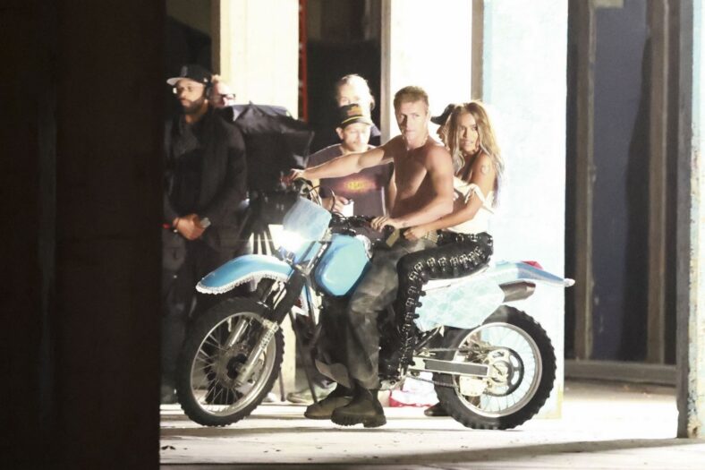 Karol G em uma motocicleta com um modelo masculino sem camisa