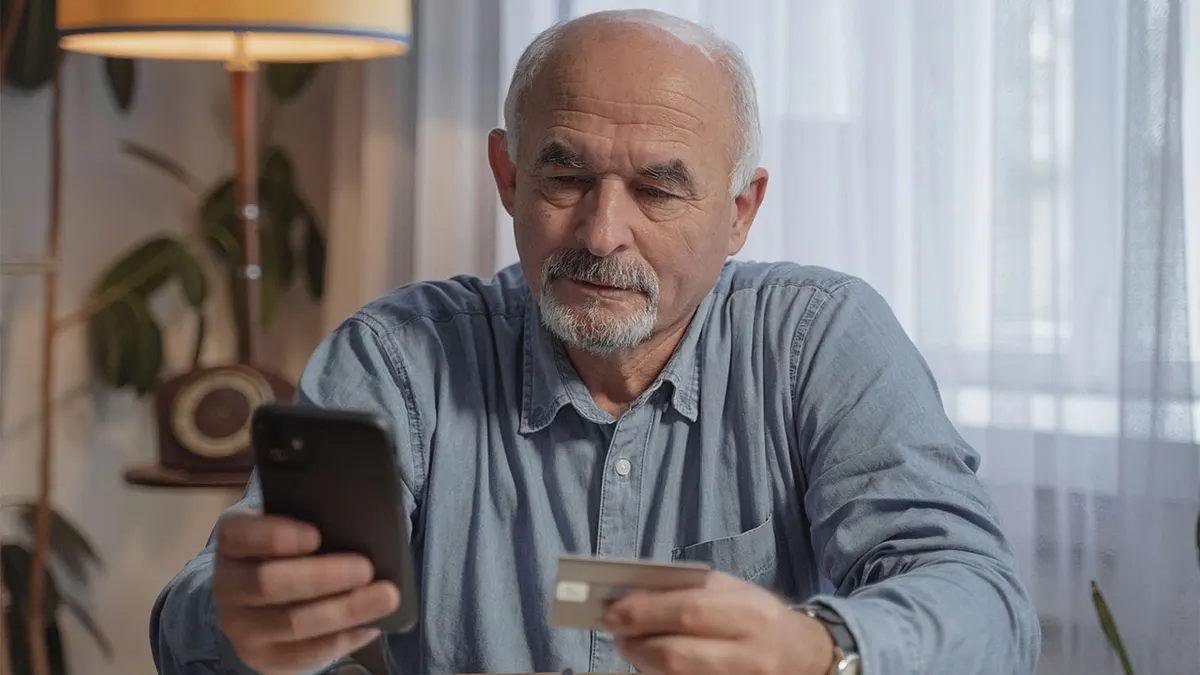 Elderly man holding credit card and phone