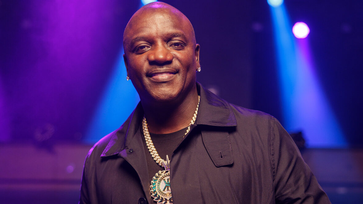 Akon vestindo uma blusa preta com um grande colar de ouro em uma gravação de videoclipe