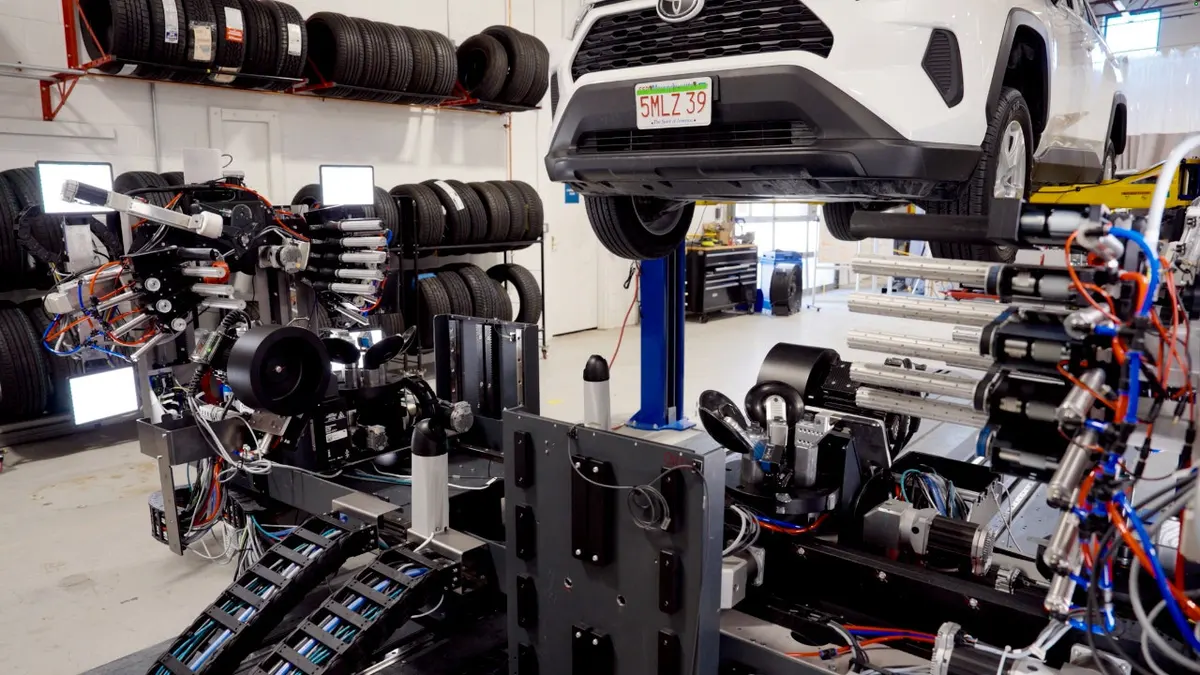 A car is elevated in a shop next to a robotic system.
