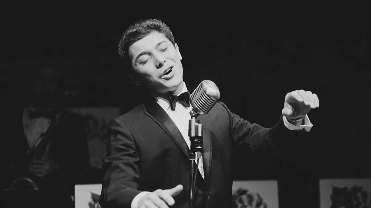 A young Paul Anka performing in a suit and bowtie on stage.