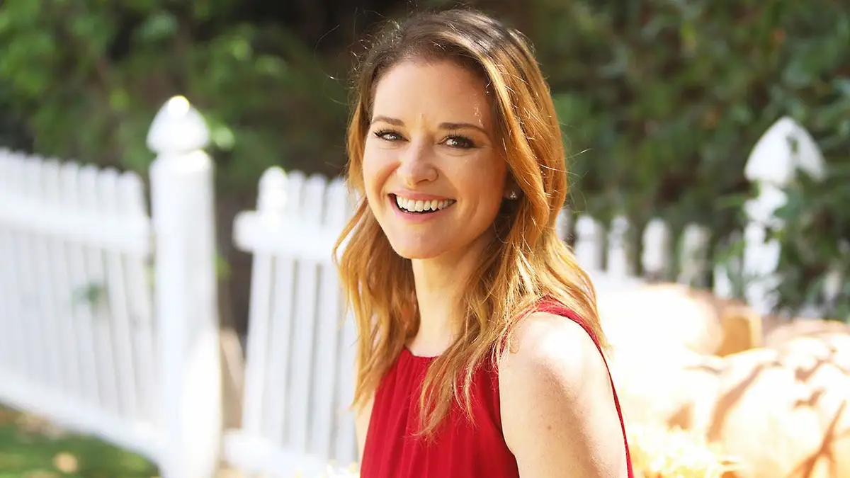 Sarah Drew wearing a red dress on a yard smiling outdoors ahead of her film premiere.