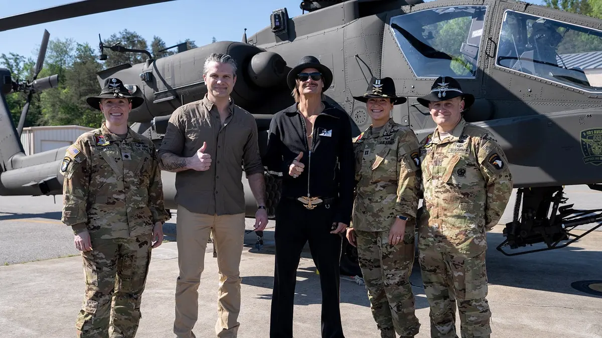Secretary of War Pete Hegseth and musician Kid Rock pose for photo with troops in front of helicopter