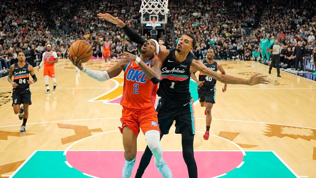Shai Gilgeous-Alexander driving to basket past Victor Wembanyama during basketball game