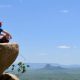 man in blue t-shirt sitting on brown rock near body of water during daytime