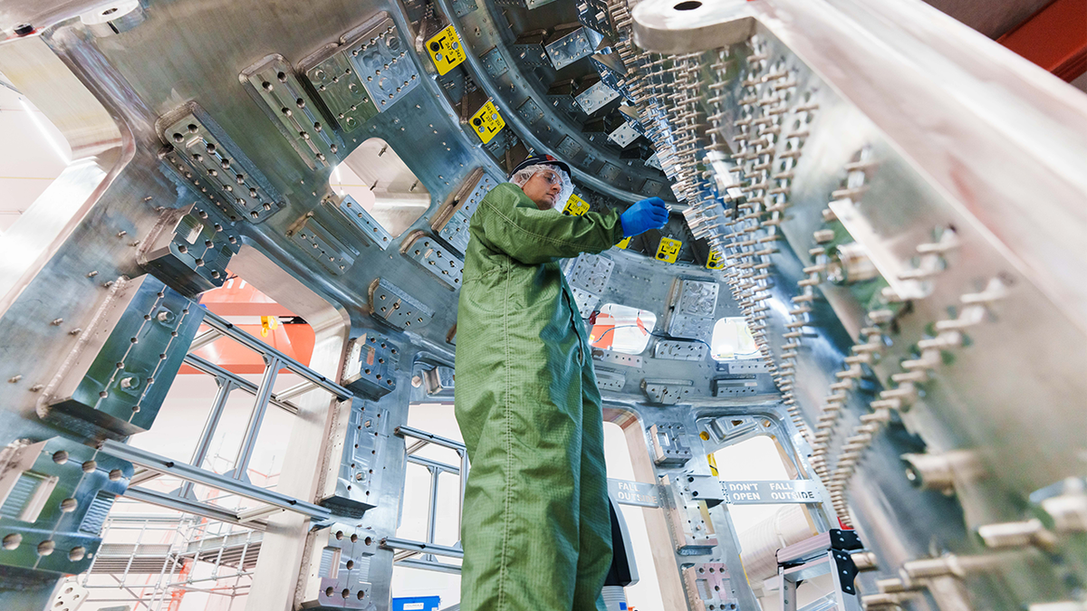 A technician wearing protective gear inspects components inside a large fusion-energy device under construction.
