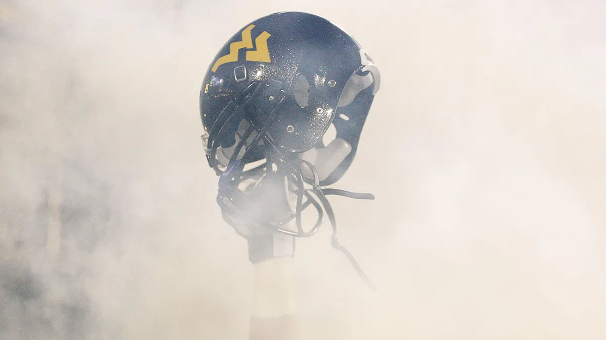 A West Virginia Mountaineers player holding up his helmet on the field.