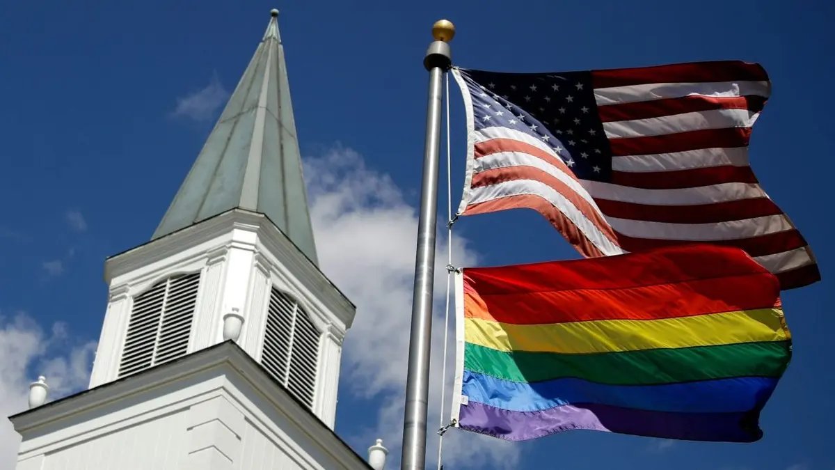 A gay Pride rainbow flag and U.S. flag flying in front of Asbury United Methodist Church