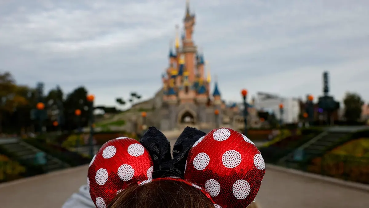A visitor wearing Mickey and Minnie Mouse ears standing in front of the Sleeping Beauty castle at Disneyland Paris