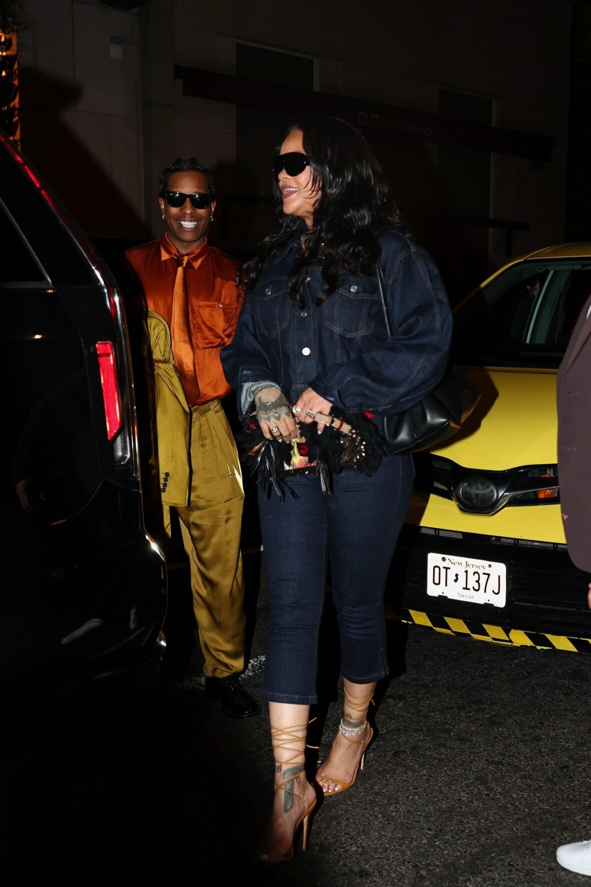 Rihanna usa jaqueta jeans escura e óculos escuros para celebrar os Knicks com A$AP Rocky, que está vestido com uma camisa de cetim e calças pregueadas