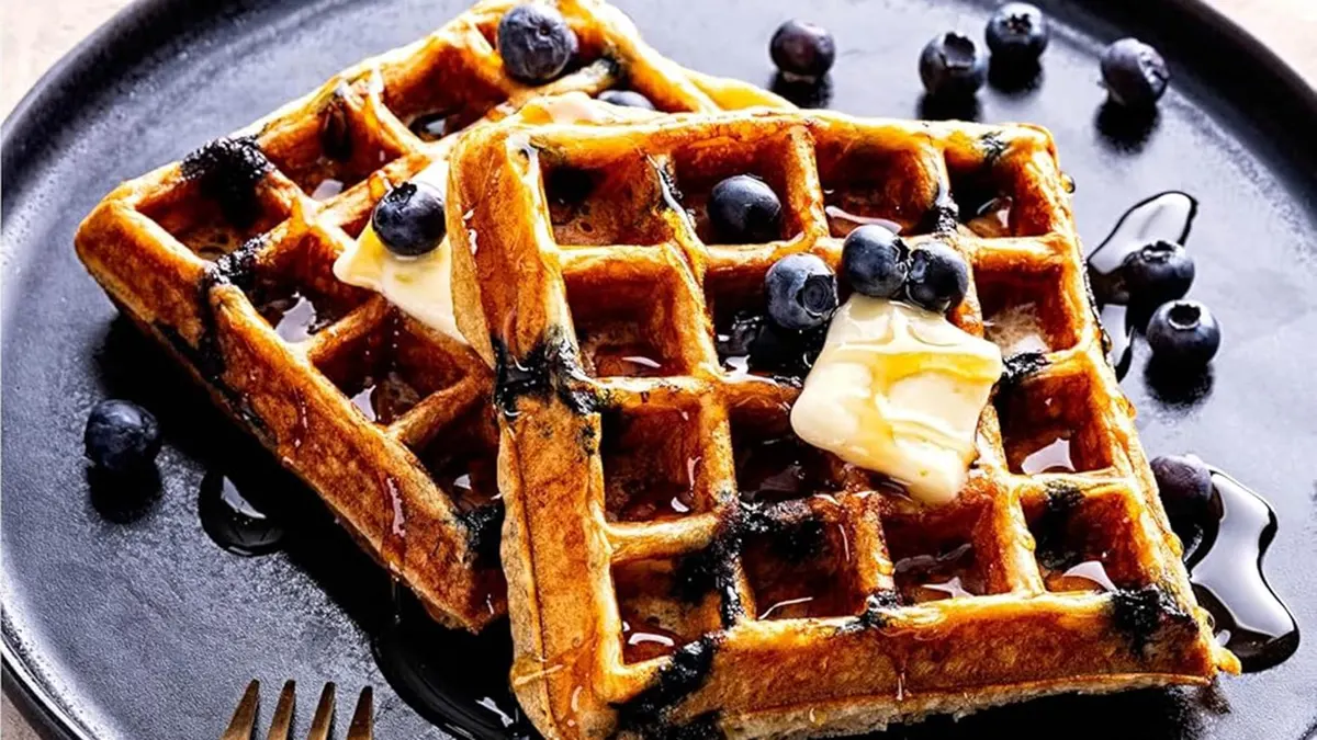 Blueberry waffles made of sourdough are shown on a plate with butter on top.