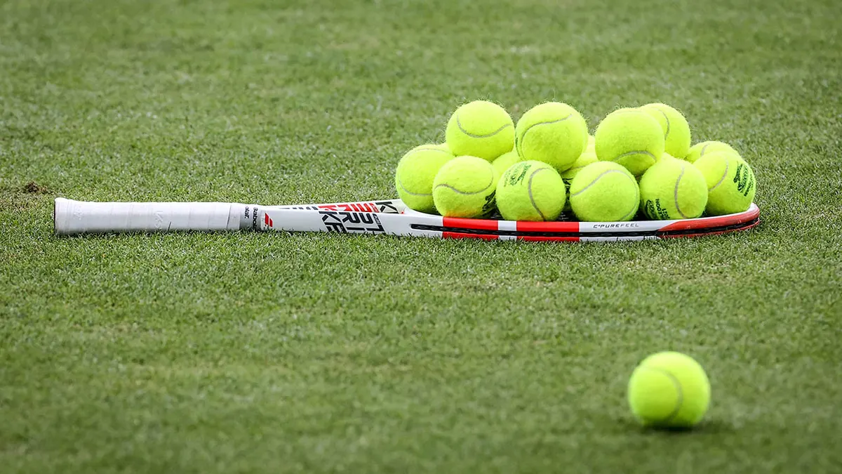 A tennis racket stacked with tennis balls on the grass at Aorangi Practice Courts.