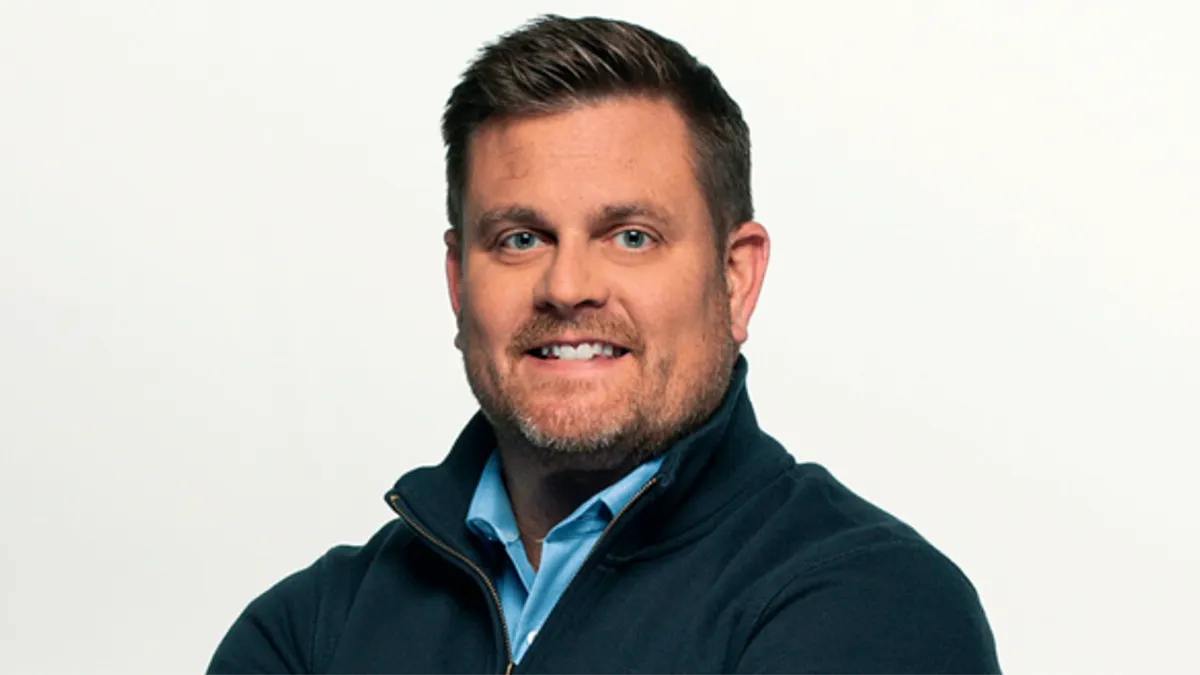 Brian Thompson smiling in a blue button down shirt and blue zip-up jacket