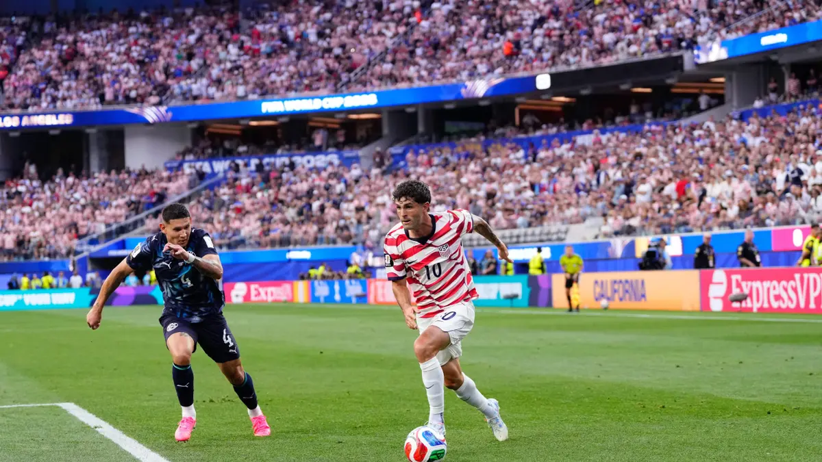 Christian Pulisic running with the ball during a soccer match at Los Angeles Stadium.
