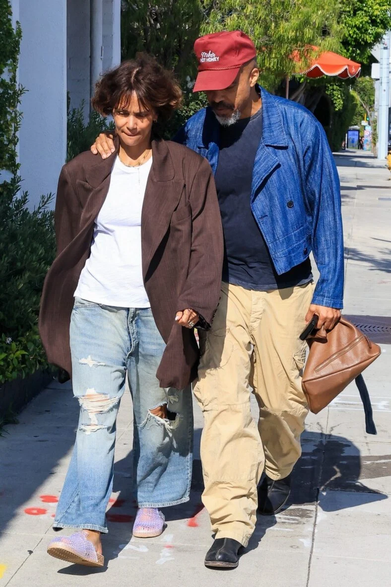 Halle Berry e o noivo Van Hunt andam de braços dados na calçada, com Van vestindo uma jaqueta azul brilhante e boné vermelho, enquanto Halle usa um blazer marrom grande e jeans
