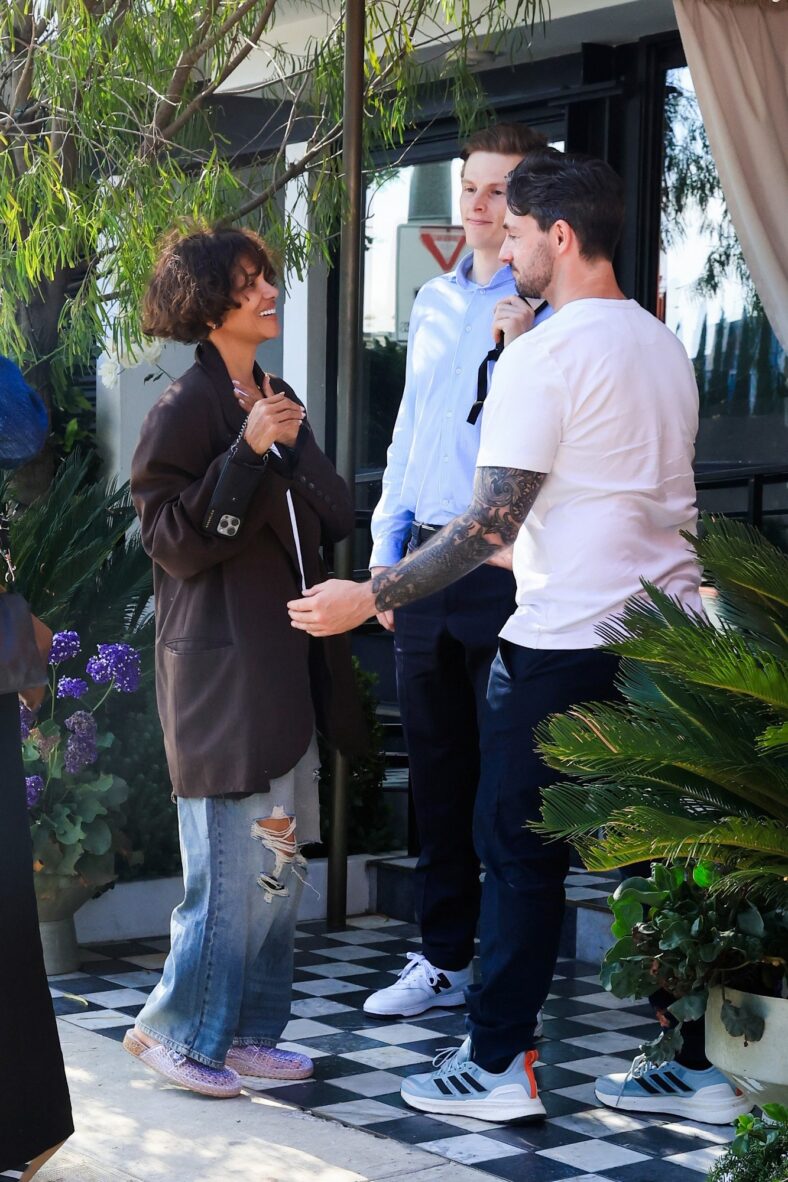 Halle Berry sorri enquanto conversa com amigos do lado de fora do The Bird Streets Club, vestindo um blazer marrom enorme, camiseta branca e jeans, durante um almoço com o noivo Van Hunt