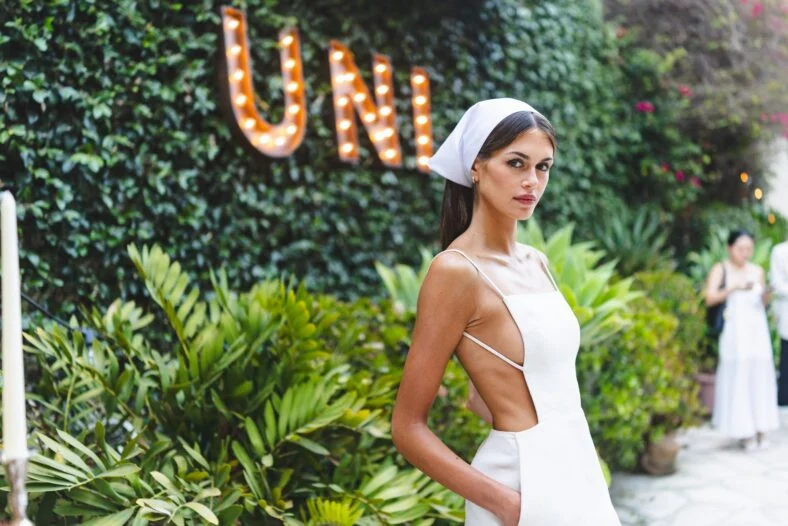 Kaia Gerber usa um minivestido branco da Calvin Klein Collection e lenço na cabeça combinando.