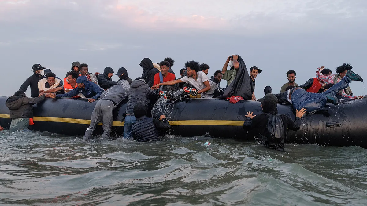 Migrants wading into water near Gravelines, France, with traffickers managing the scene