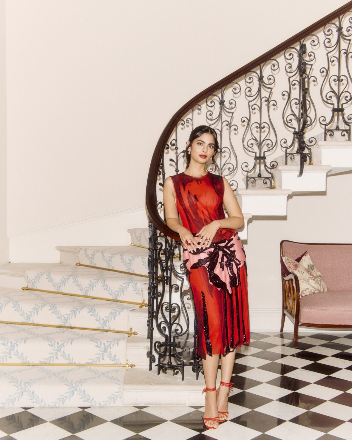 Isha Ambani em um vestido vermelho perto de uma escada em espiral