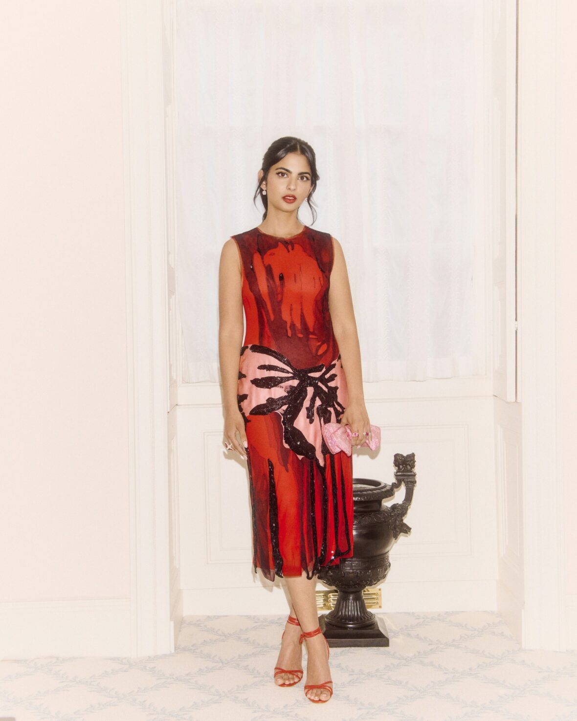 Isha Ambani em um vestido vermelho perto de uma escada em espiral