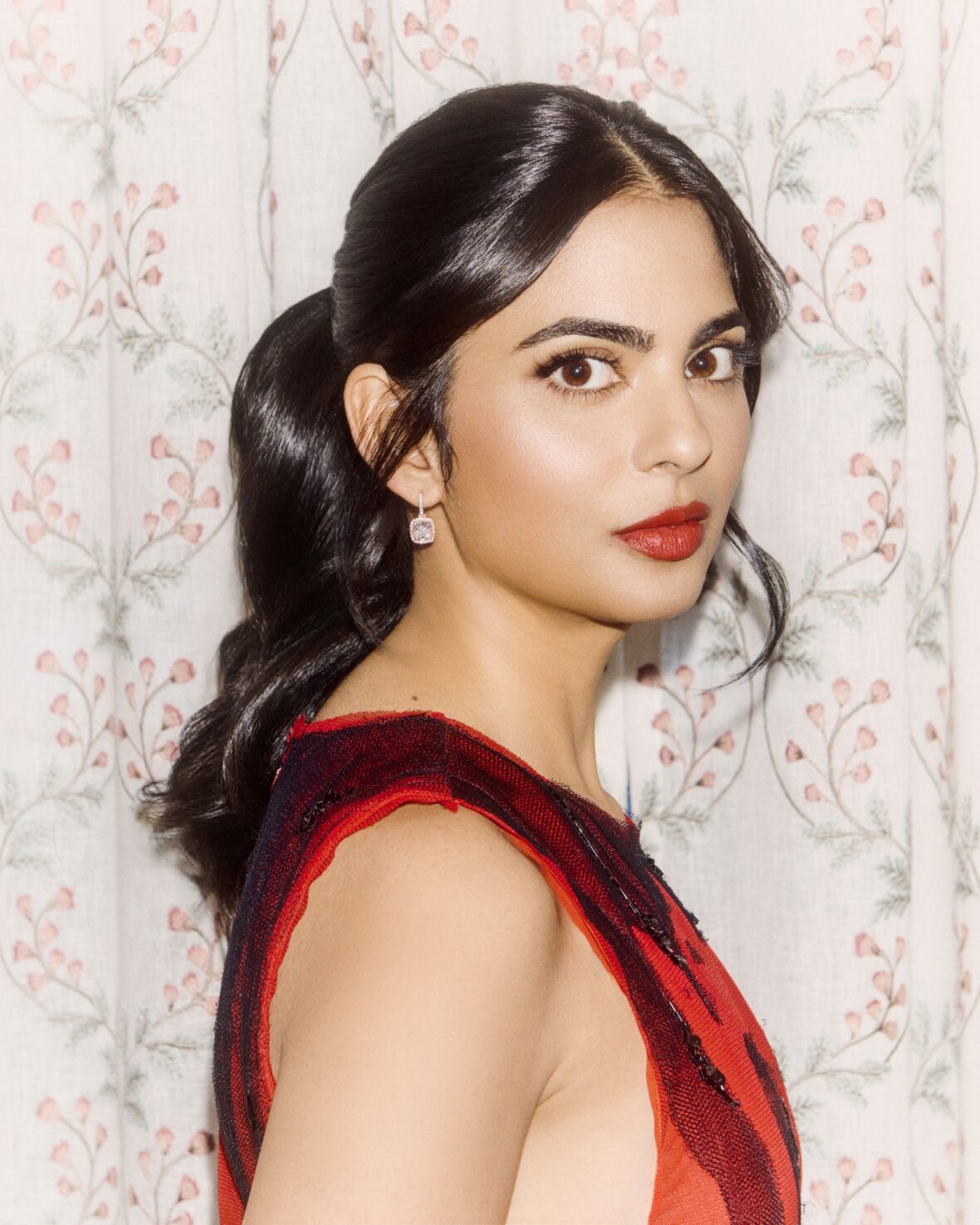 Isha Ambani em um vestido vermelho perto de uma escada em espiral