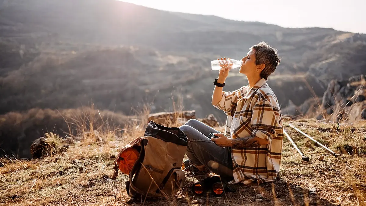 A woman hiker stops for a drink in an arid environment.