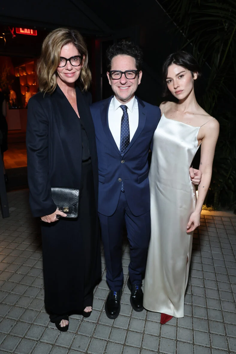 Katie McGrath, JJ Abrams e Gracie Abrams posam juntos em um evento, com Gracie usando um vestido branco justo.