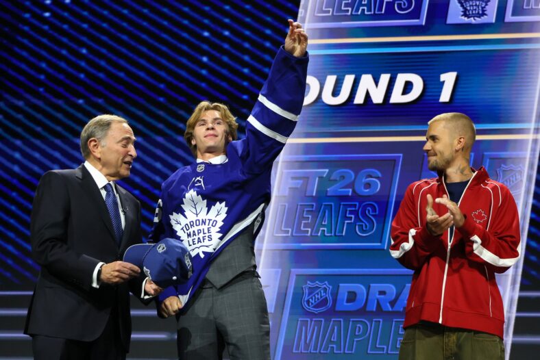 O comissário da NHL, Gary Bettman, entrega o chapéu a Gavin McKenna, do Canadá, enquanto o cantor Justin Bieber observa McKenna