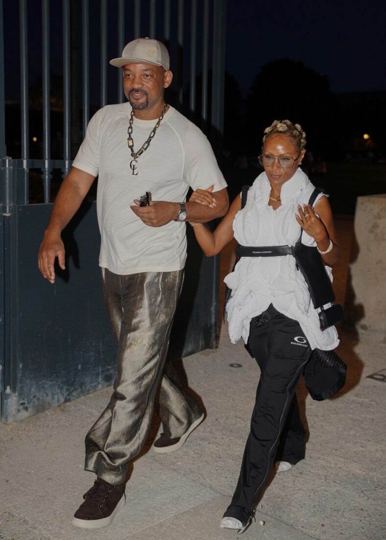 Will Smith sorri enquanto caminha de braços dados com Jada Pinkett Smith após um raro jantar em Paris.