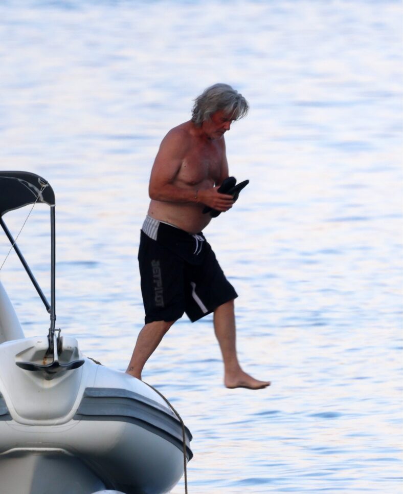 Kurt Russell sem camisa em um barco enquanto pula na água.