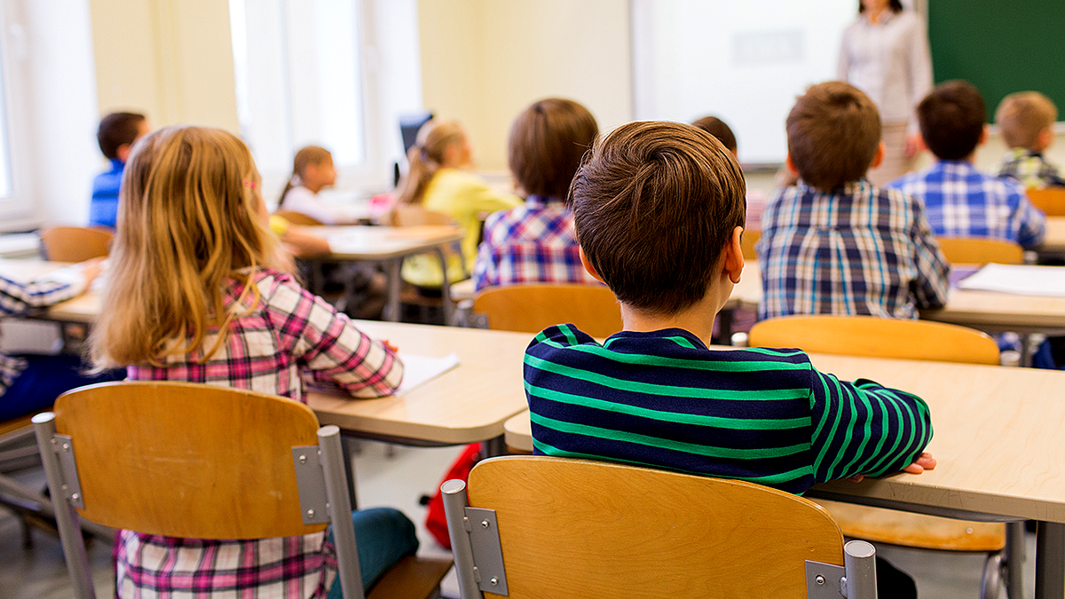 Elementary school teacher standing in classroom with seated first-grade students