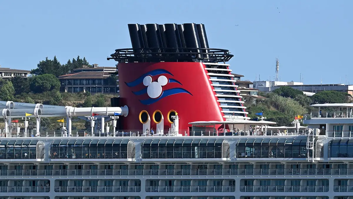 Disney Fantasy cruise ship with Mickey Mouse logo on smokestack sailing on Tagus River in Lisbon