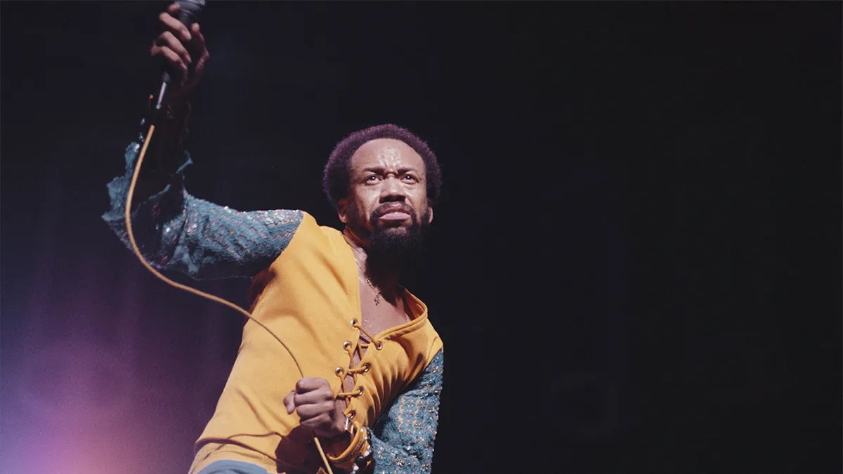 Maurice White singing and playing drums on stage.