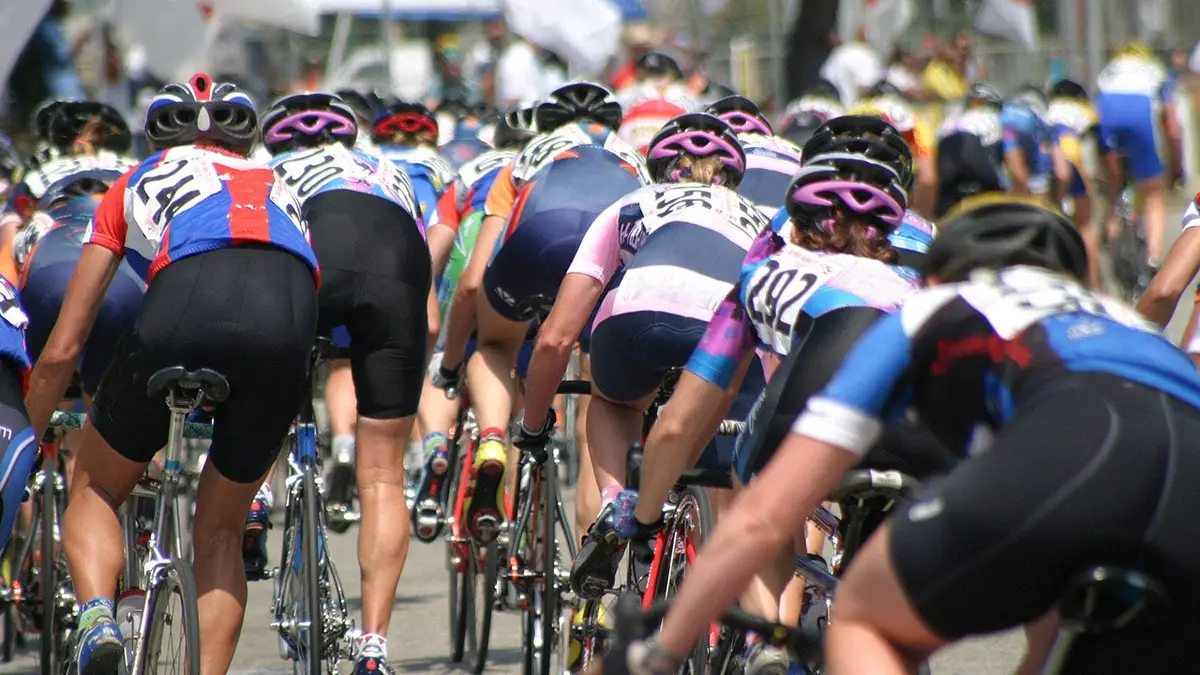 A peloton of cyclists riding closely together on a road.