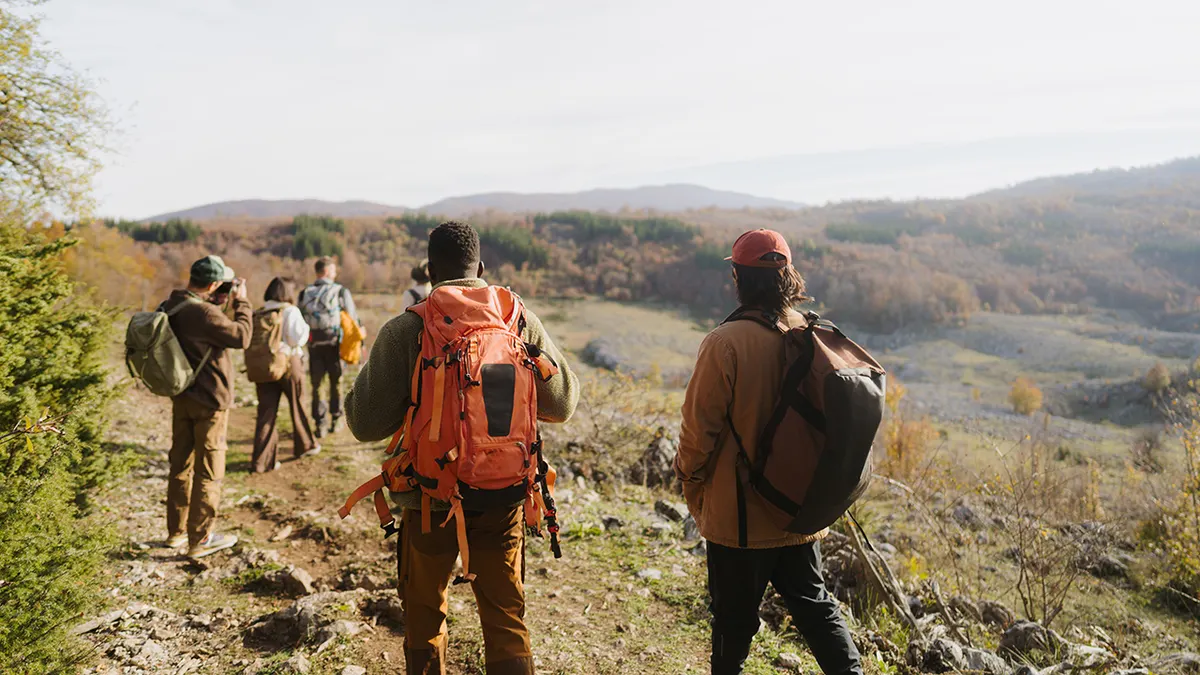 A diverse group of hikers walking along a mountain trail with backpacks.