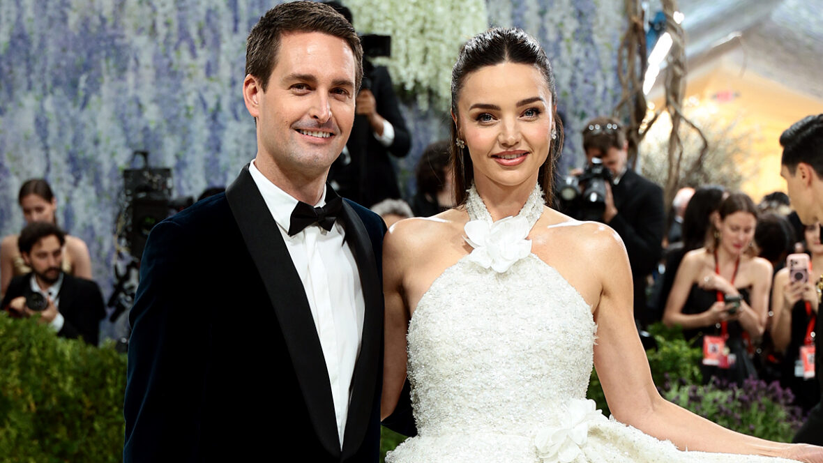 Evan Spiegel e Miranda Kerr posam juntos no tapete vermelho do Met Gala, com Miranda usando um vestido branco e Evan um smoking preto.